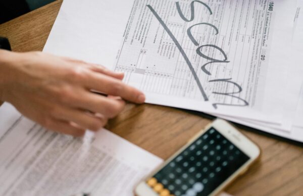 pexels-photo-7247408-7247408 Close-up of hands examining documents marked 'scam' with a calculator nearby.